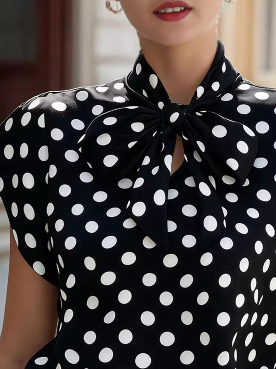 Black polka dot blouse with a bow neckline worn by a person.