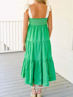 Woman wearing a green dress with white straps on a wooden deck.