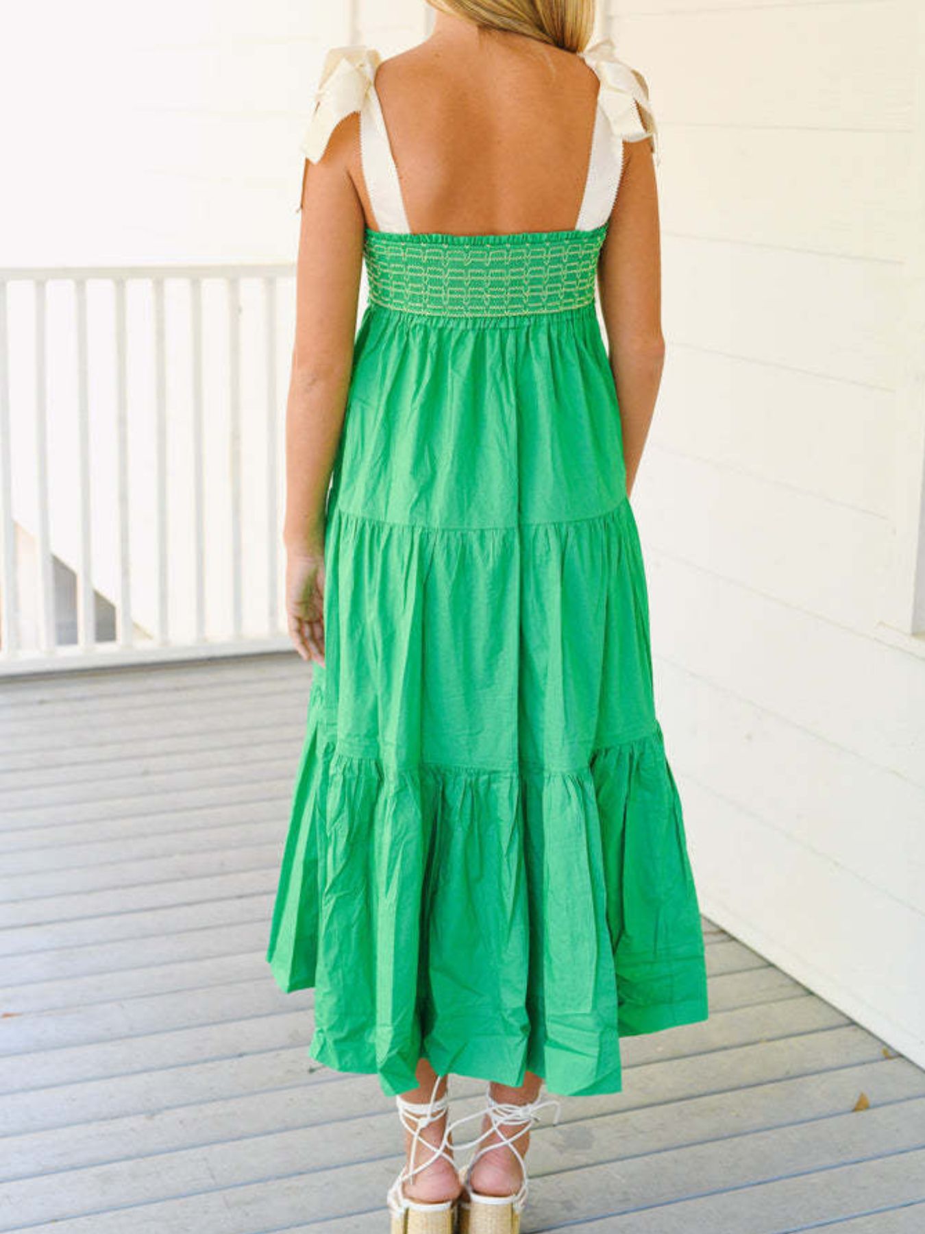 Woman wearing a green dress with white straps on a wooden deck.
