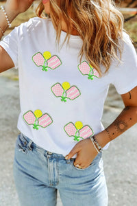Person wearing a white t-shirt with colorful designs on a blurred natural background