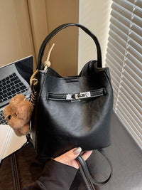 Black handbag held by a person with a laptop and teddy bear in the background
