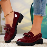 Red patent leather shoes with black soles worn by a person on a blurred background
