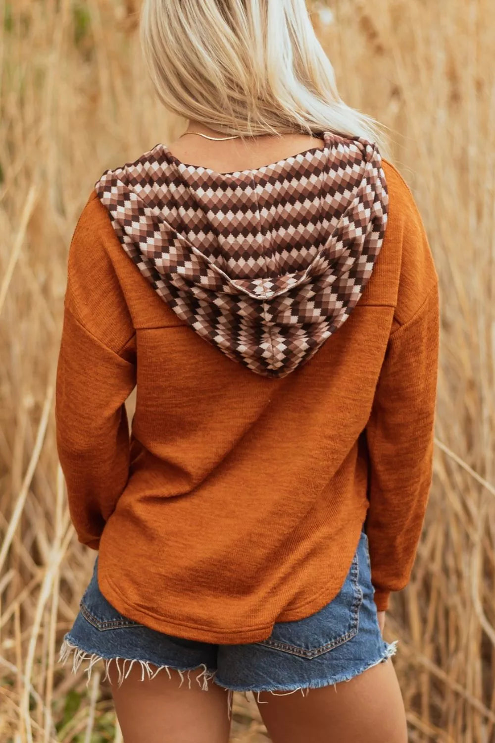 Person wearing a brown hoodie with a patterned hood in a field of tall grass.