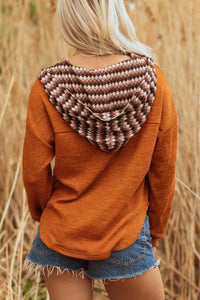 Person wearing a brown hoodie with a patterned hood in a field of tall grass.