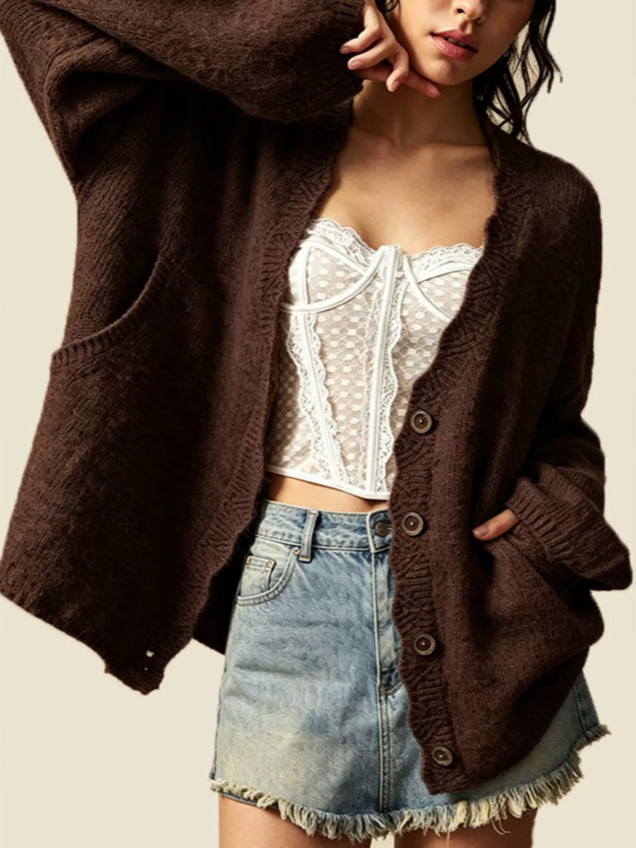 A woman wearing a dark brown chunky knit cardigan over a white lace-trim camisole and a light blue denim mini skirt, photographed against a plain light beige background.