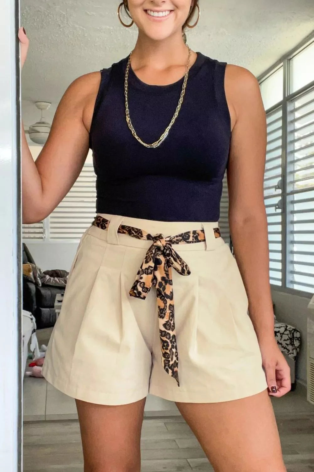 Woman wearing a navy top and beige shorts with a leopard print belt in a room.