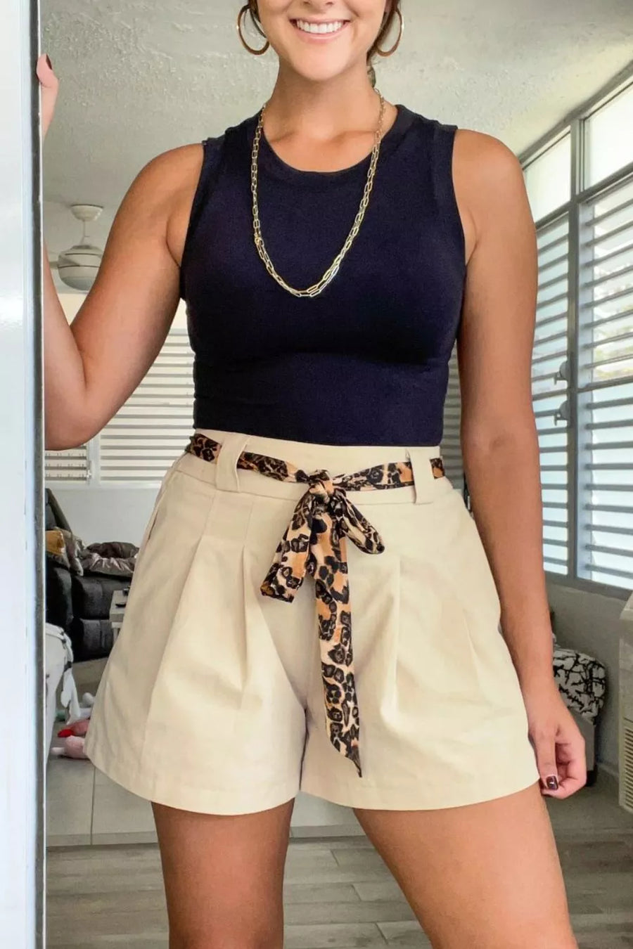 Woman wearing a navy top and beige shorts with a leopard print belt in a room.