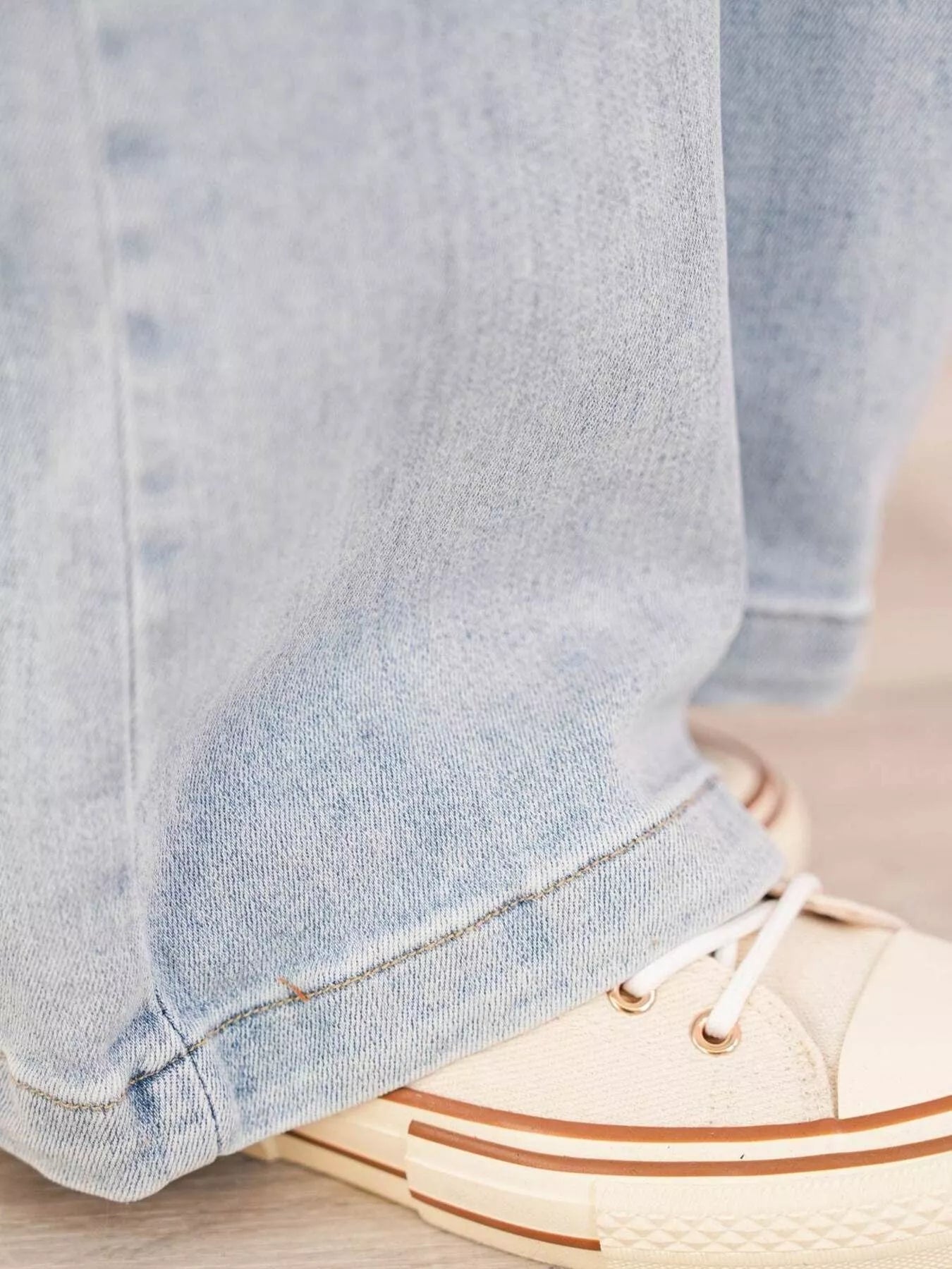 Close-up of light blue jeans and beige sneakers with brown stripes on a neutral background