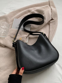 Black handbag held by a hand with red nail polish on a light background