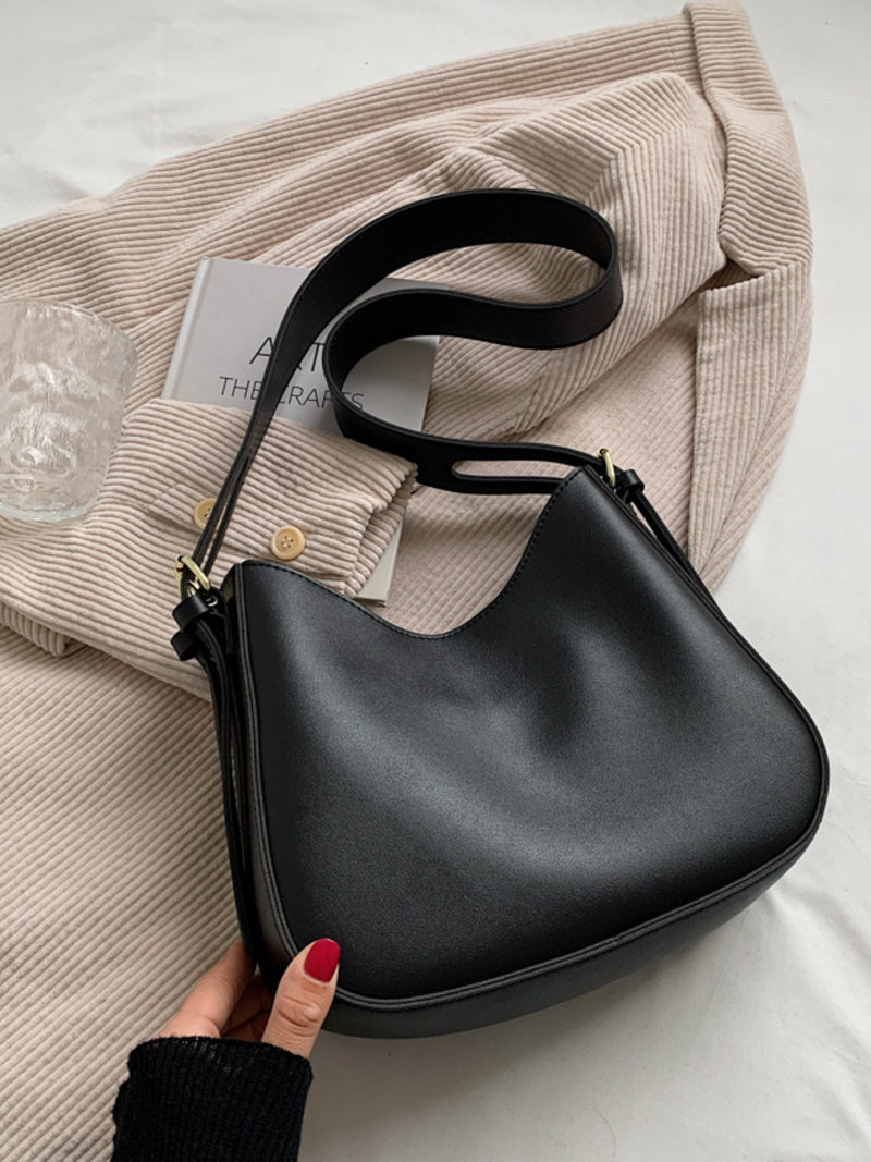 Black handbag held by a hand with red nail polish on a light background