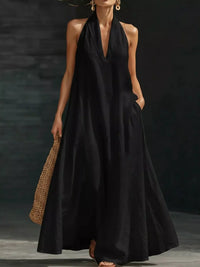 Woman wearing a black halter neck dress holding a woven bag against a dark background