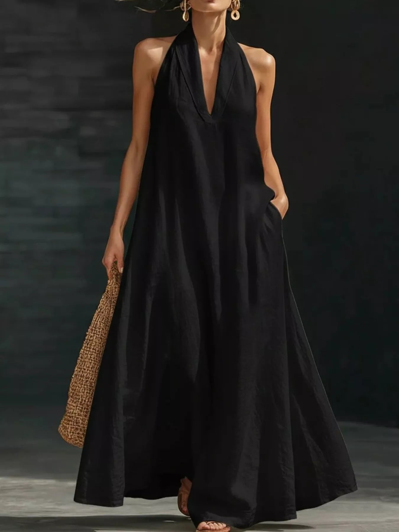 Woman wearing a black halter neck dress holding a woven bag against a dark background