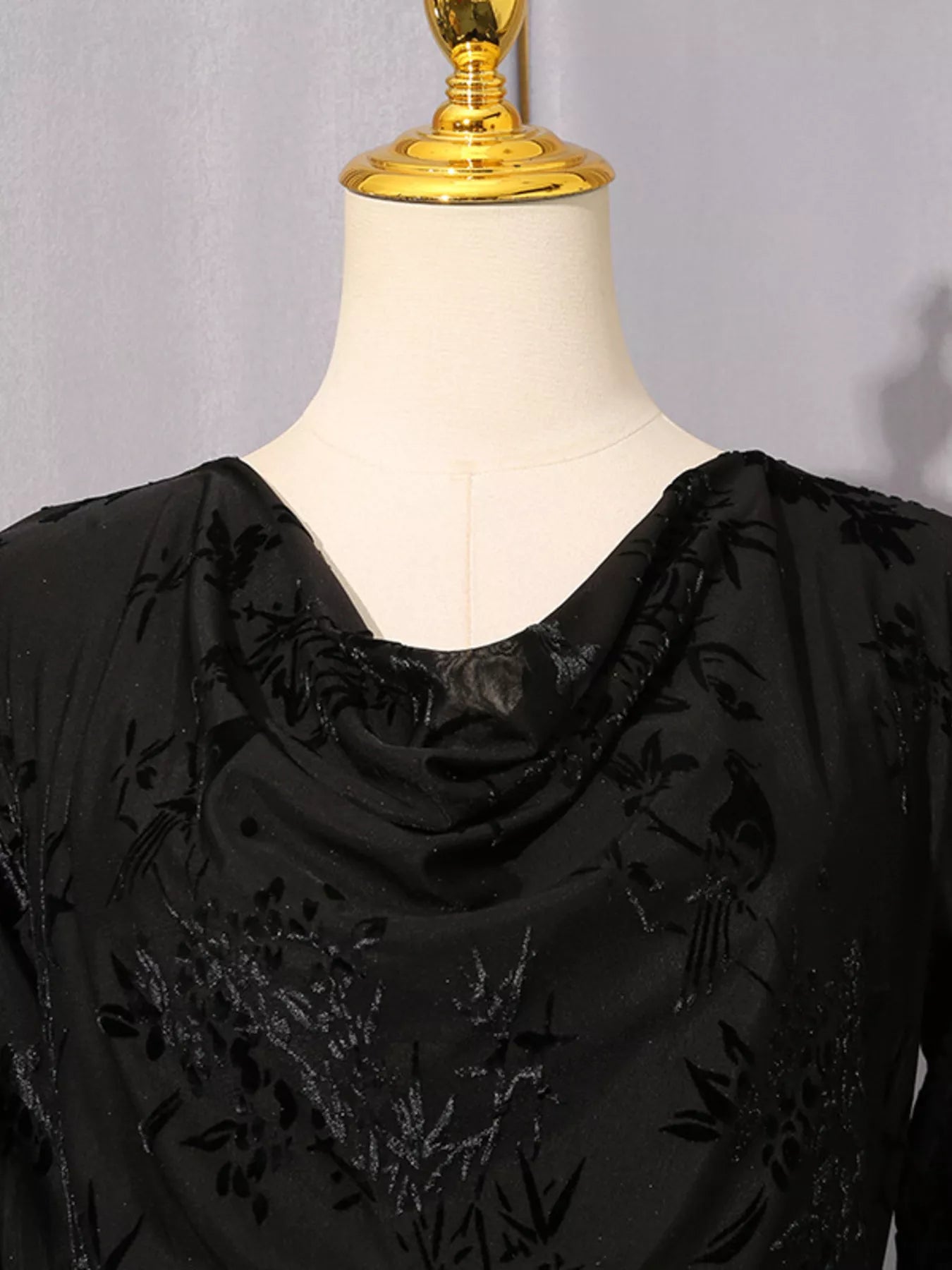 Black cowl neck blouse with tonal floral embroidery, displayed on a cream dress form with a gold neck cap.