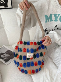 Colorful pom-pom bag held by a person on a white couch