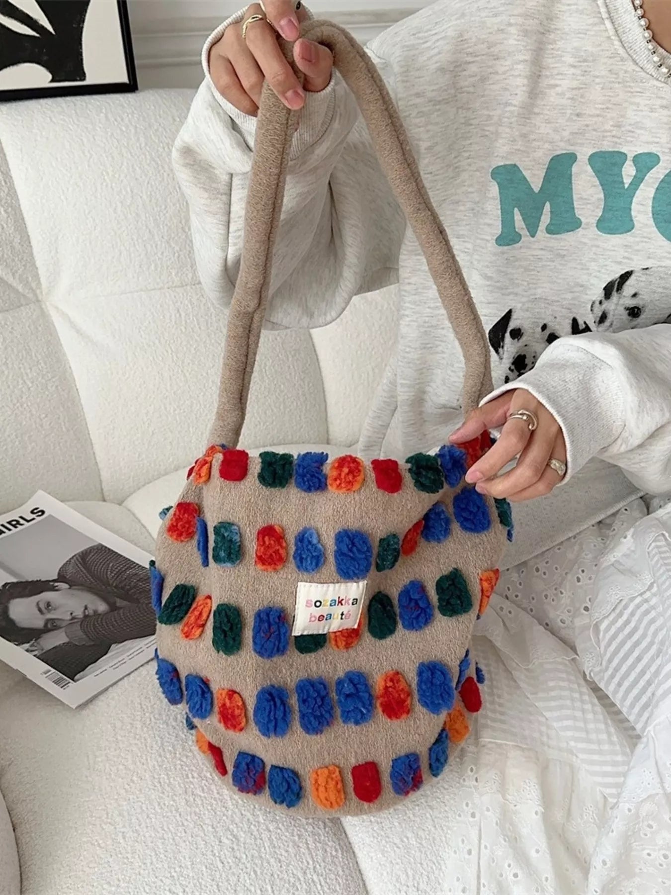 Colorful pom-pom bag held by a person on a white couch