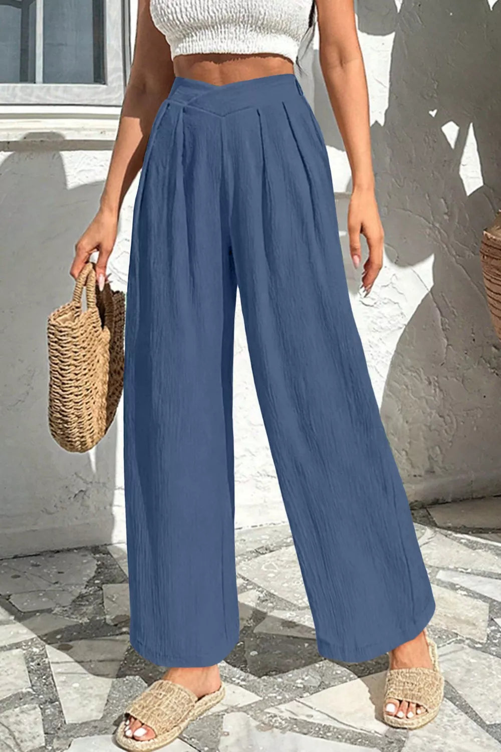 Person wearing blue wide-leg pants and a white top, standing on a stone pavement.