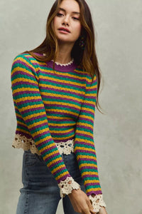Woman wearing a colorful striped sweater with lace cuffs against a neutral background