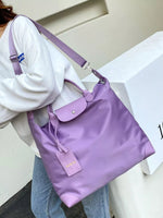 Person holding a purple handbag with a visible brand logo against a neutral background