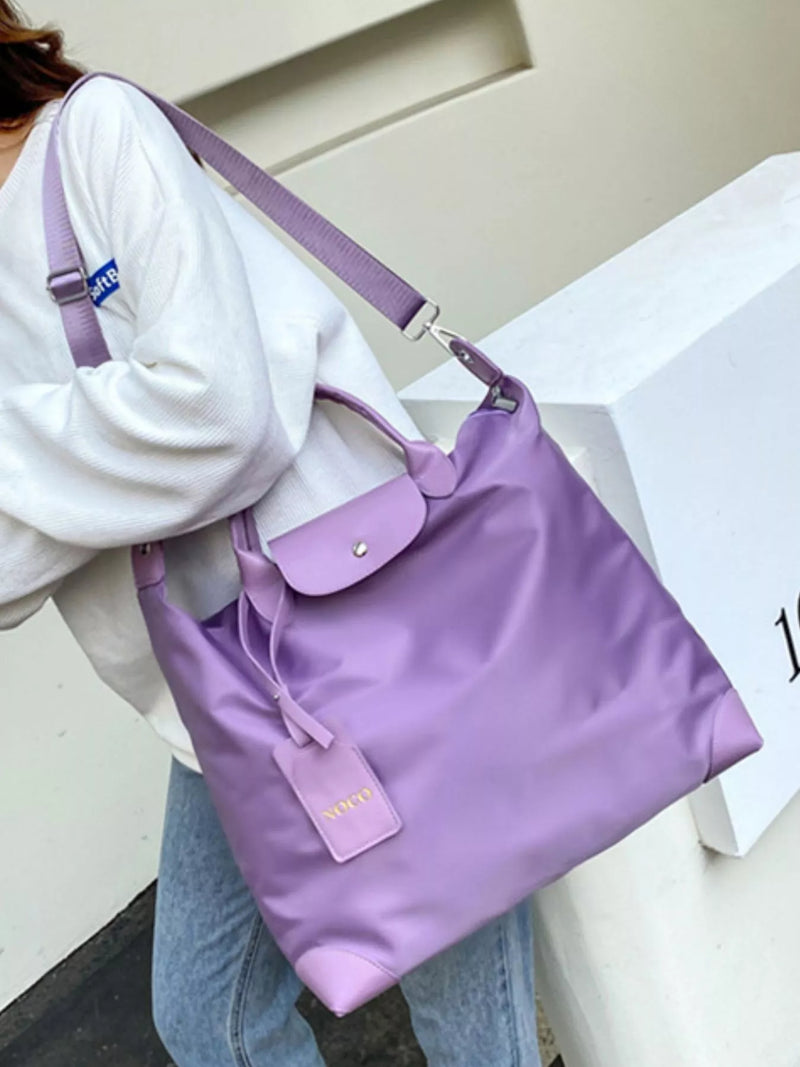 Person holding a purple handbag with a visible brand logo against a neutral background