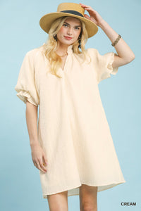 Woman wearing a cream dress and straw hat against a light blue background