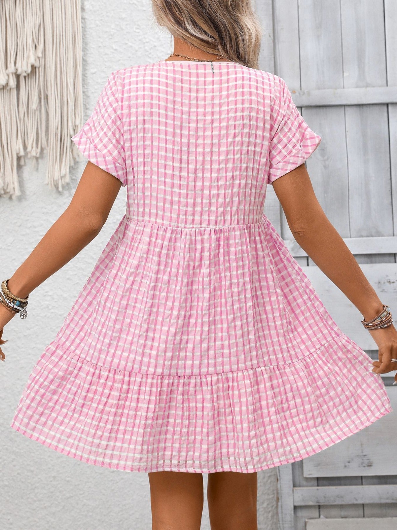 Person wearing a pink checkered dress against a light gray wall.