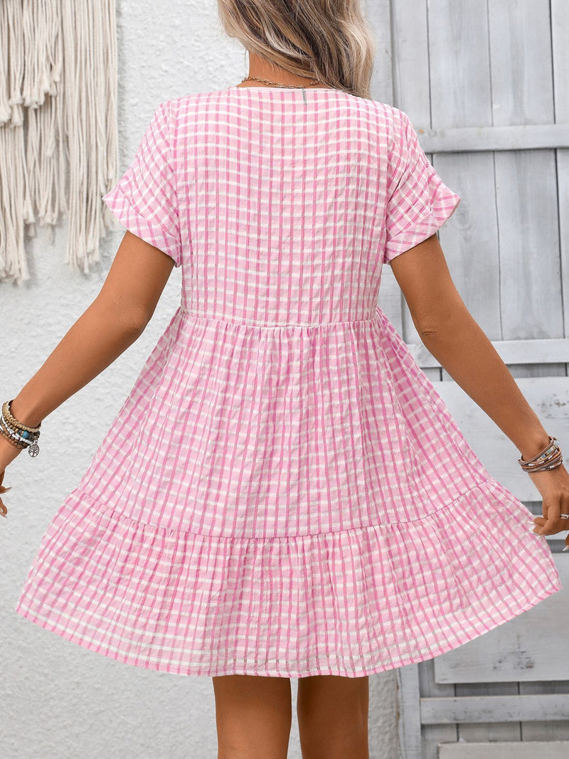 Person wearing a pink checkered dress against a light gray wall.