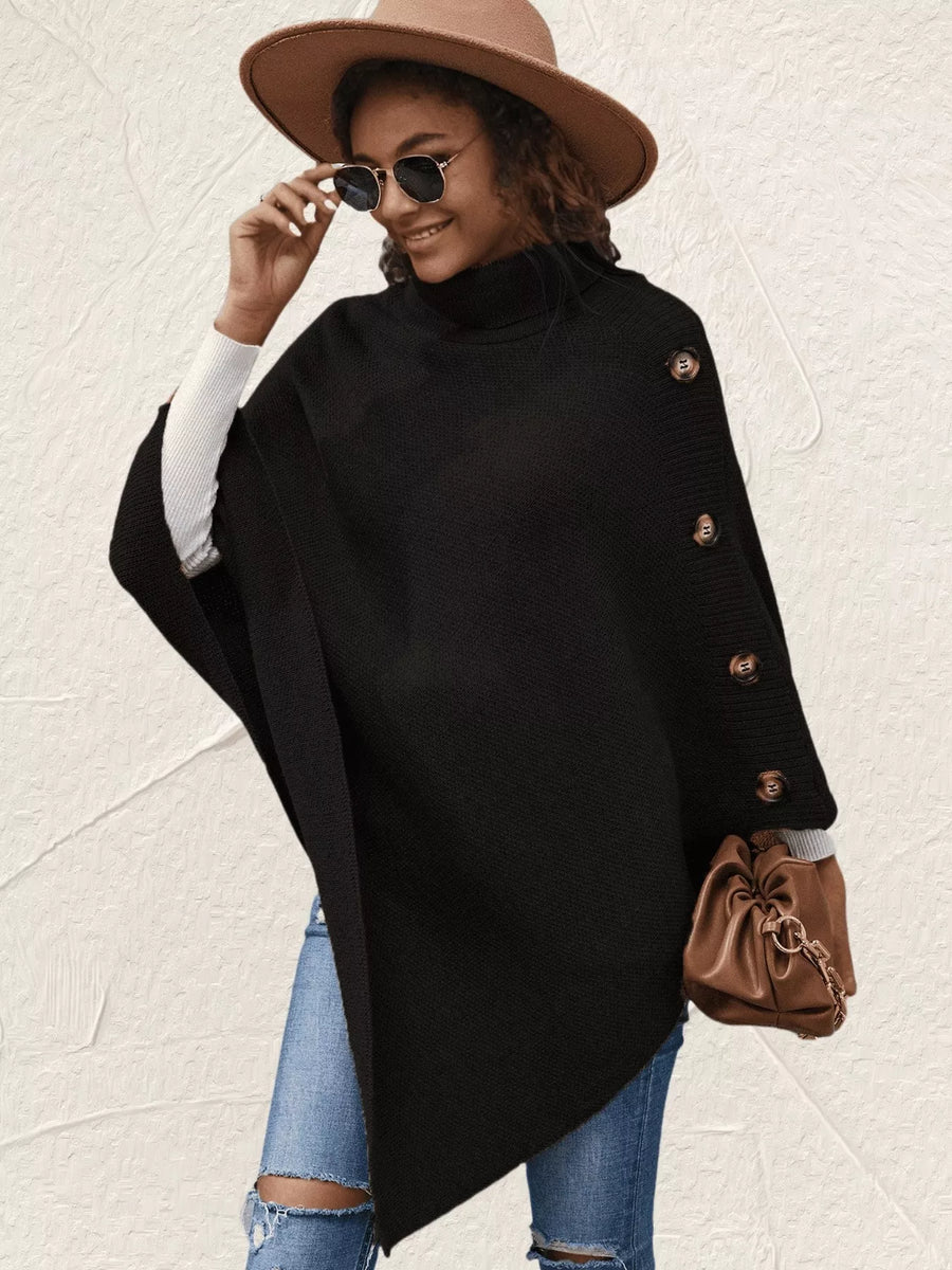 Woman wearing a black poncho with buttons, blue jeans, and a brown hat on a light background
