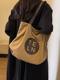 Person wearing a beige tote bag with 'TEL'N' logo on a plain background