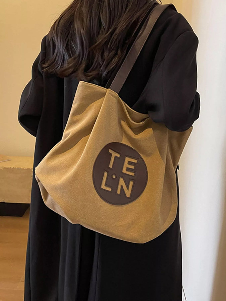 Person wearing a beige tote bag with 'TEL'N' logo on a plain background