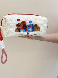 Quilted pouch with embroidered dog design held by a hand against a plain background