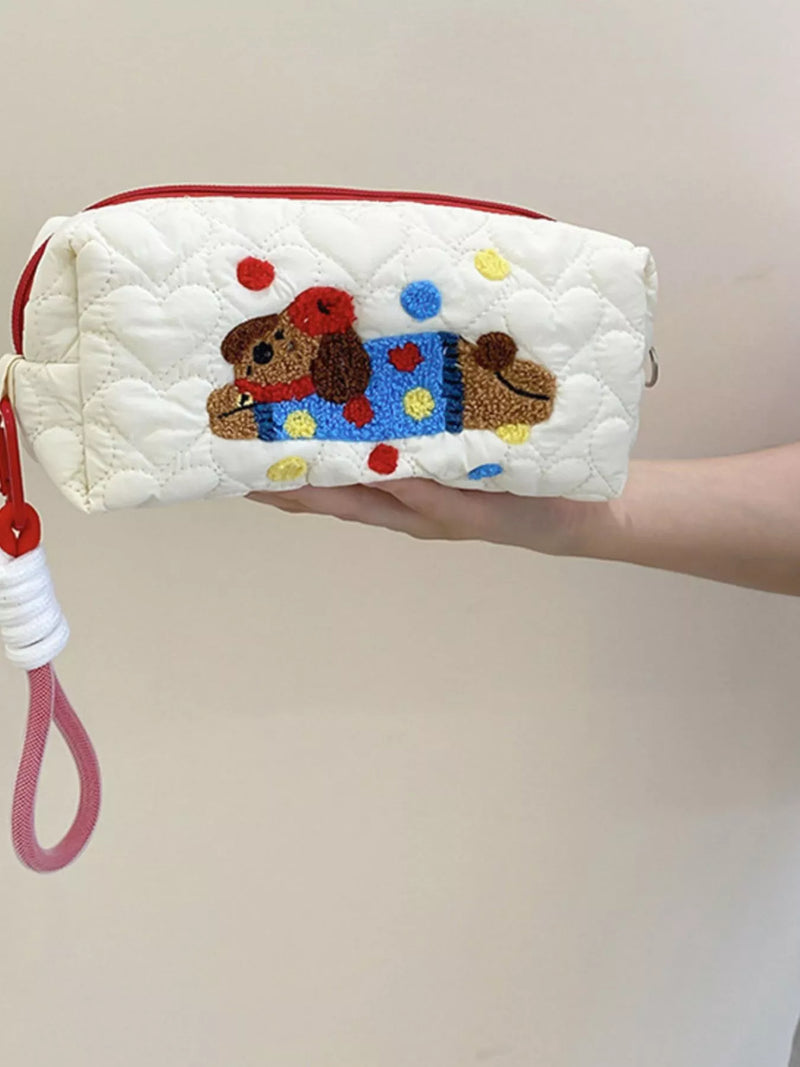 Quilted pouch with embroidered dog design held by a hand against a plain background