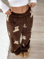 Brown fleece pants with bear pattern worn by a person on a wooden floor.
