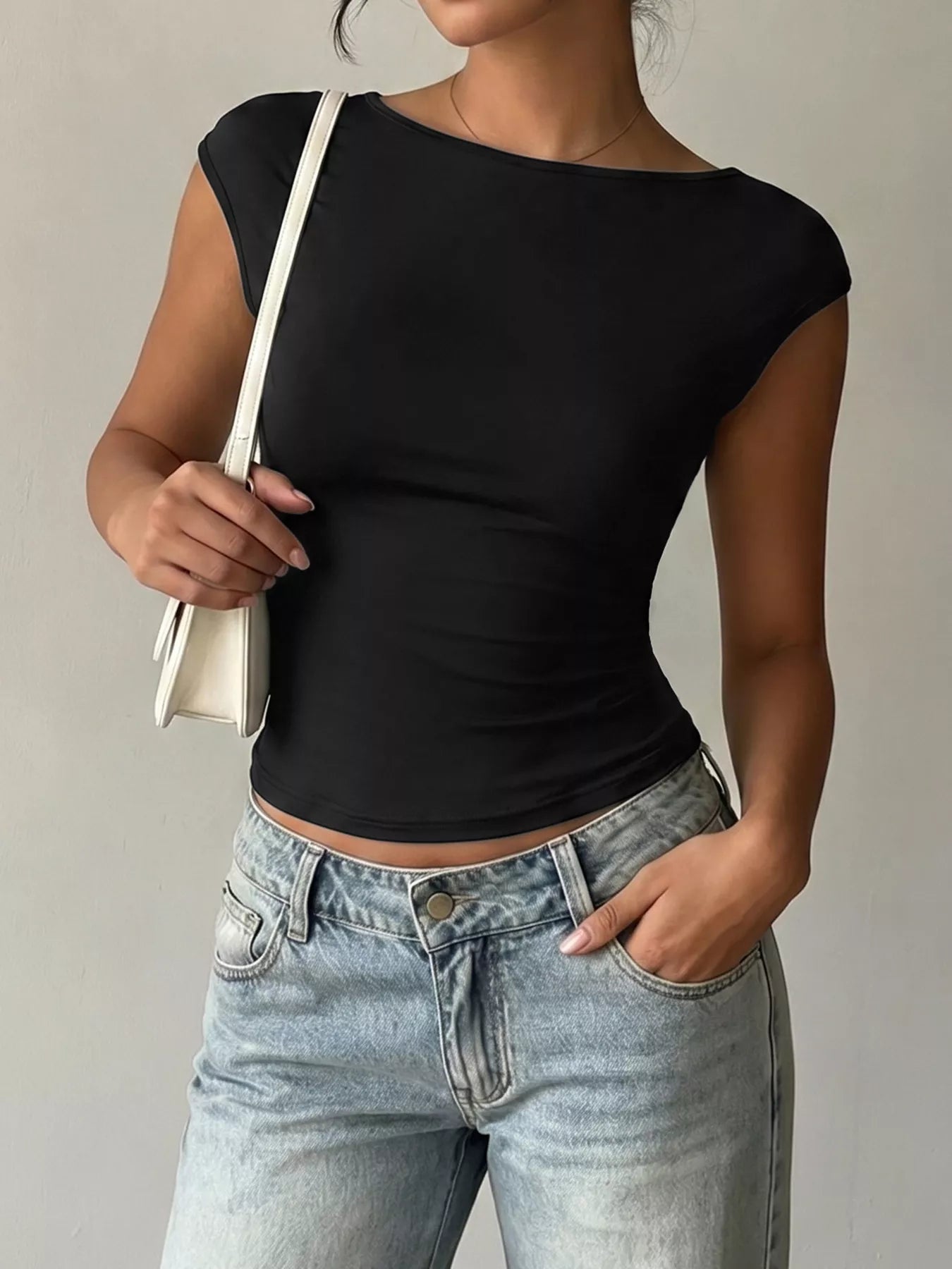 Person wearing a black top and light blue jeans holding a white bag against a neutral background