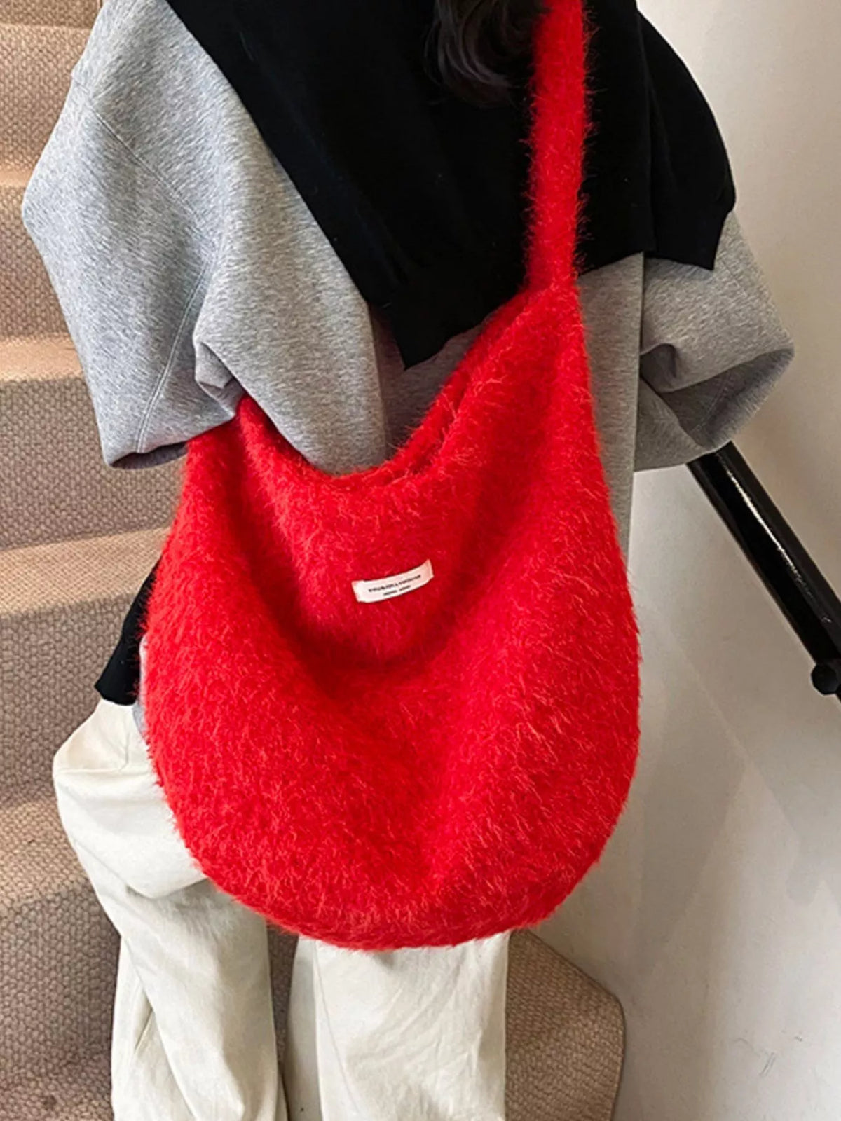 Red textured handbag held by a person wearing a black and gray outfit.