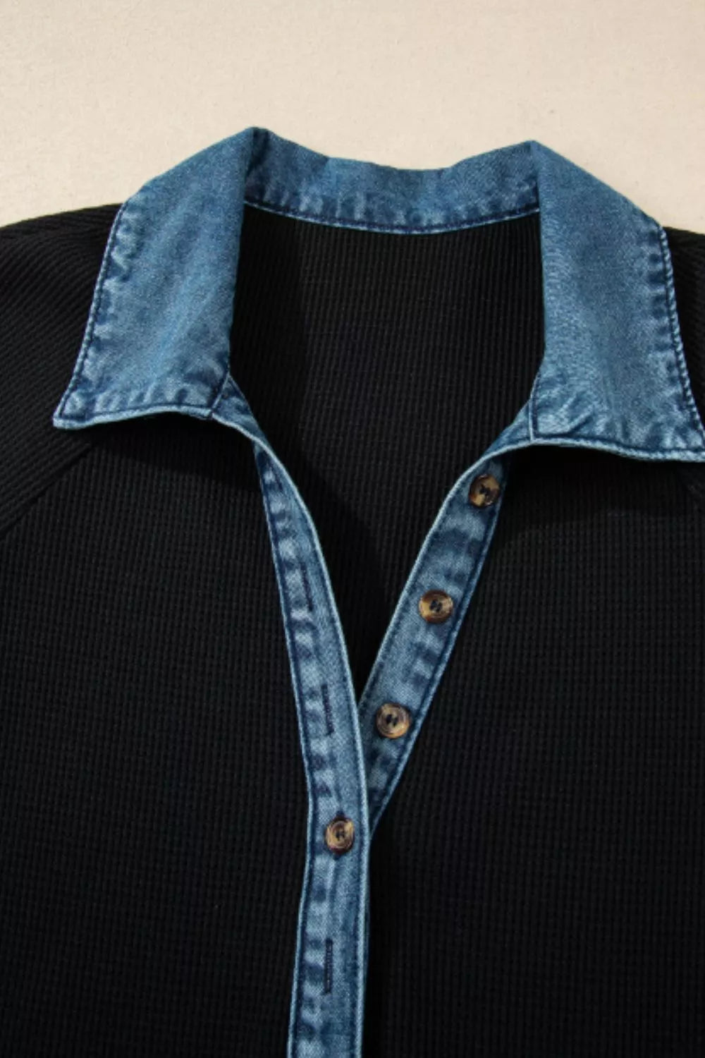 Black shirt with blue denim collar and buttons on a beige background
