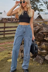 Woman wearing a black crop top and blue jeans standing near a stone wall outdoors.