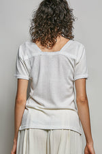 Person wearing a light-colored textured top and pants against a plain background