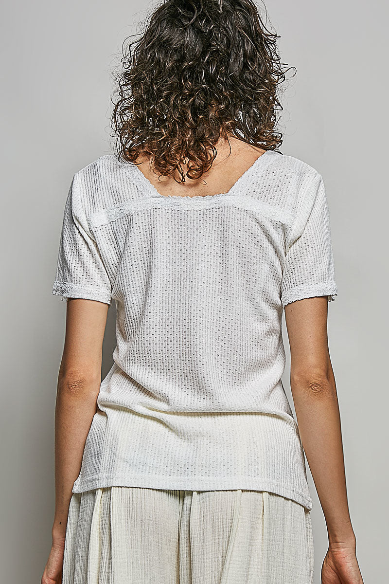 Person wearing a light-colored textured top and pants against a plain background