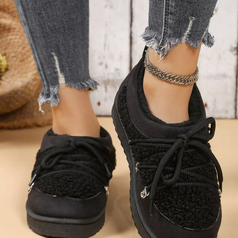 Black sneakers worn with ripped jeans on a neutral background