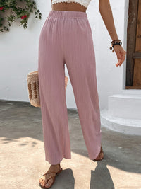 Person wearing pink wide-leg pants with a white wall and plant in the background