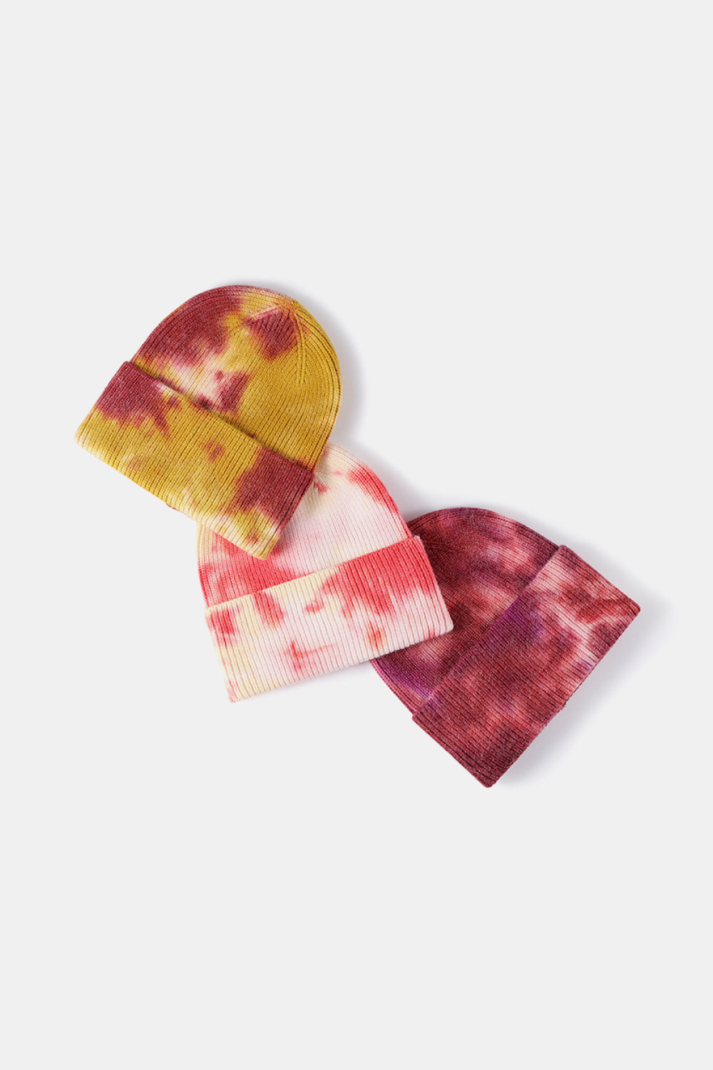 Three tie-dye beanies in yellow, pink, and red on a white background