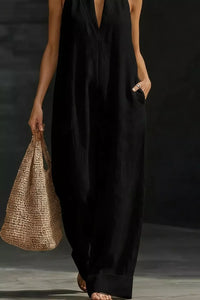 Person wearing a black sleeveless dress holding a woven bag against a dark background