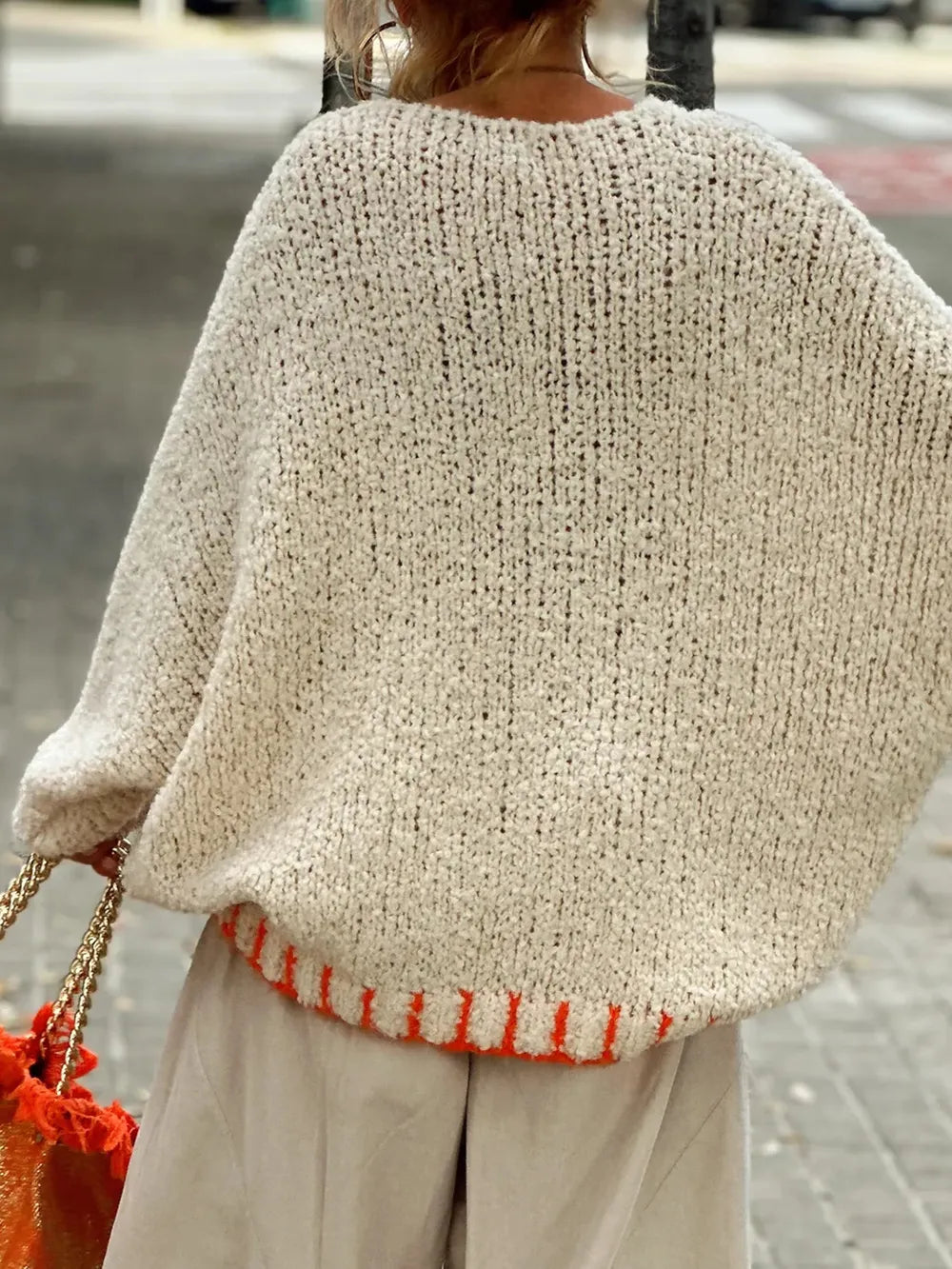 Person wearing a beige knitted poncho with a red accent on a blurred street background