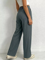 Person wearing teal wide-leg pants against a white brick wall.