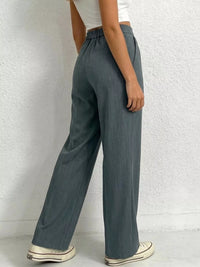 Person wearing teal wide-leg pants against a white brick wall.