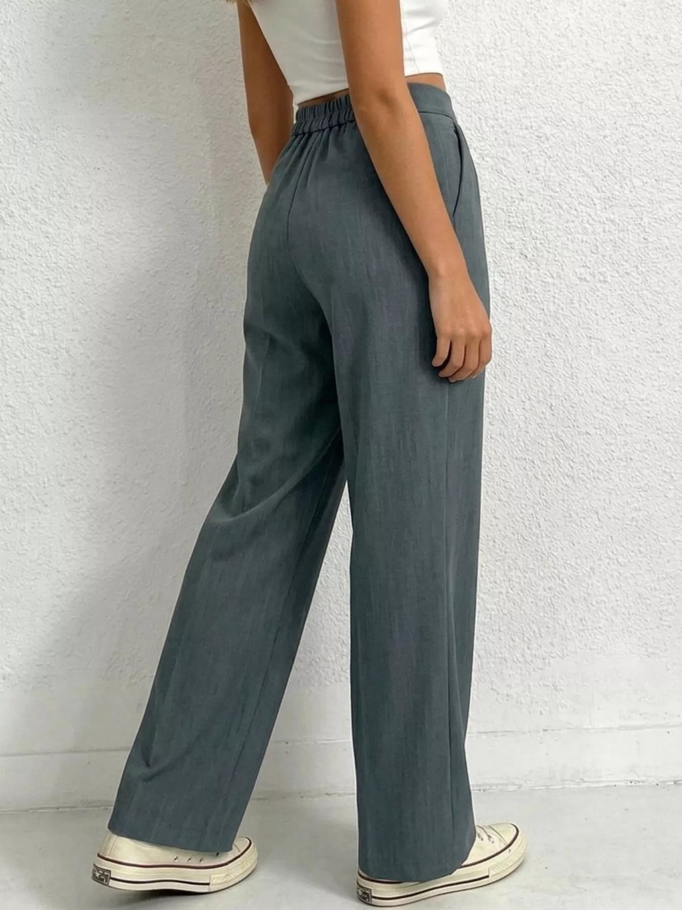 Person wearing teal wide-leg pants against a white brick wall.
