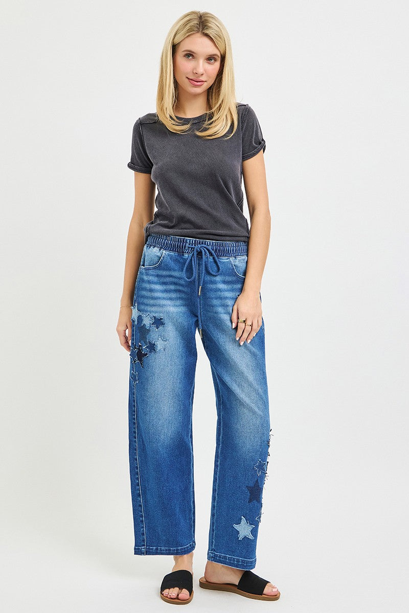 Woman wearing a gray t-shirt and blue jeans with star patterns on a white background