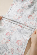 Floral-patterned fabric held by hands against a neutral background