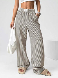 Person wearing striped wide-leg pants holding a white bag on a plain background