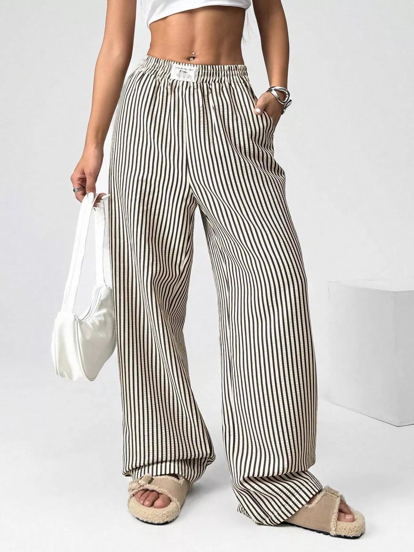 Person wearing striped wide-leg pants holding a white bag on a plain background